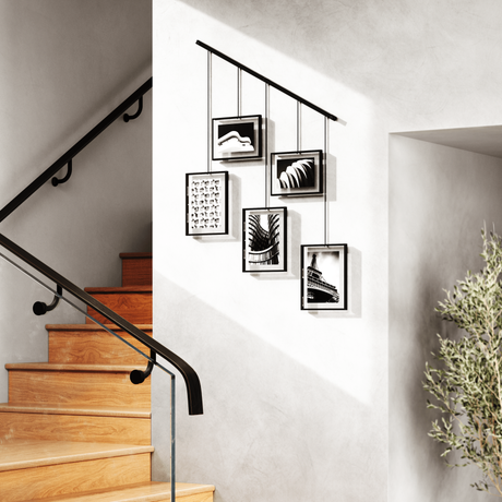 Five black photo frames hung on wires from a rod beside a staircase